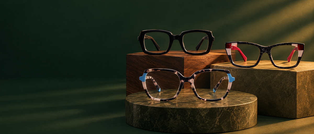 Allure, Ellis and Amalia Berkley eyeglasses on walnut and olive stone plinths, lit by warm amber light against deep emerald.